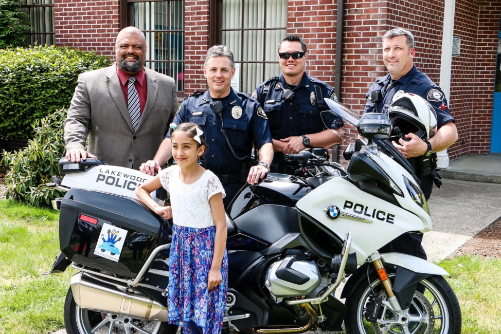 Tillicum Elementary School second grader Iyaat T. with Ron Banner, Mike Zaro and two Lakewood Police officers. Iyaat was one of the winners of the CPSD-LPD Kids Art Contest.