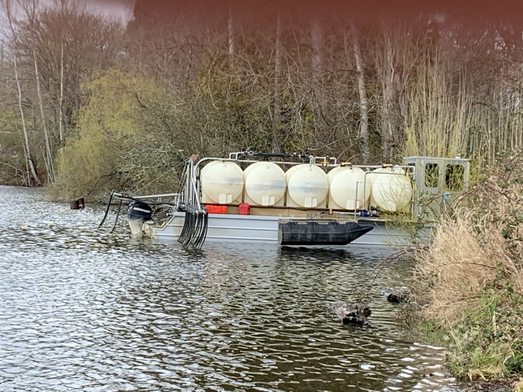 A boat with five white barrels on top to administer alum treatment in Waughop Lake in Lakewood, WA