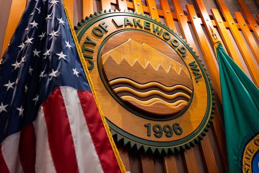 A photo of the American Flag and Washington state flag in the Lakewood City Council Chambers with the City Seal hanging on the wall