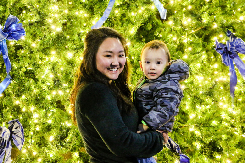 A woman holds a child in front of the city Christmas tree