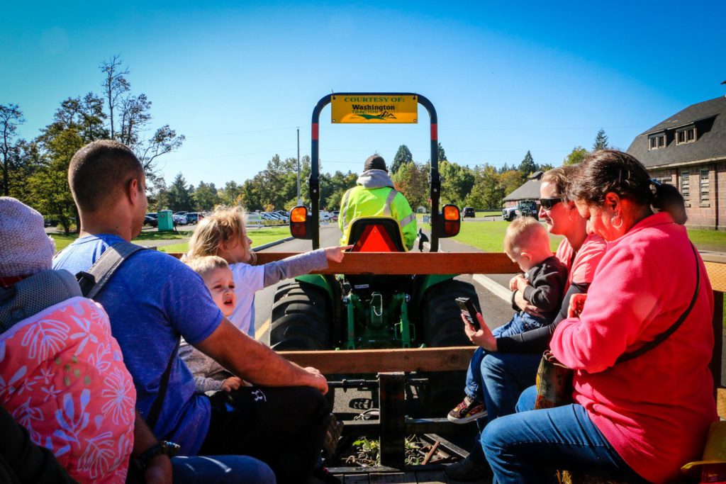 A group of people sit in the back of a hay ride on a sunny day. 