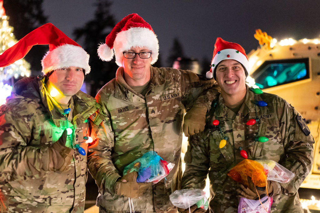 A group of active duty military members smile wearing santa hats and Christmas light lighted neckalces