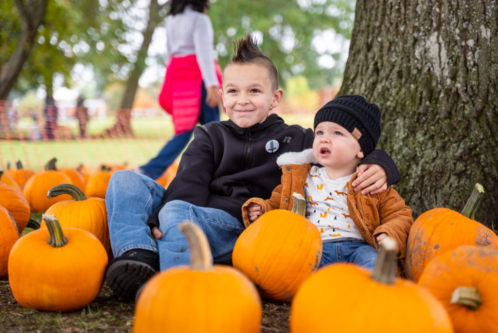 Two children posing for a picture sit among pumpkins at the base of a tree at Lakewood's Truck & Tractor Day
