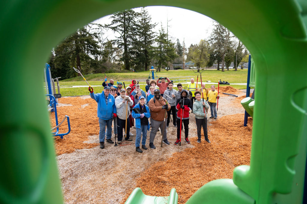 A group of volunteers smiles as the photographer takes a photo of them through the playset. 
