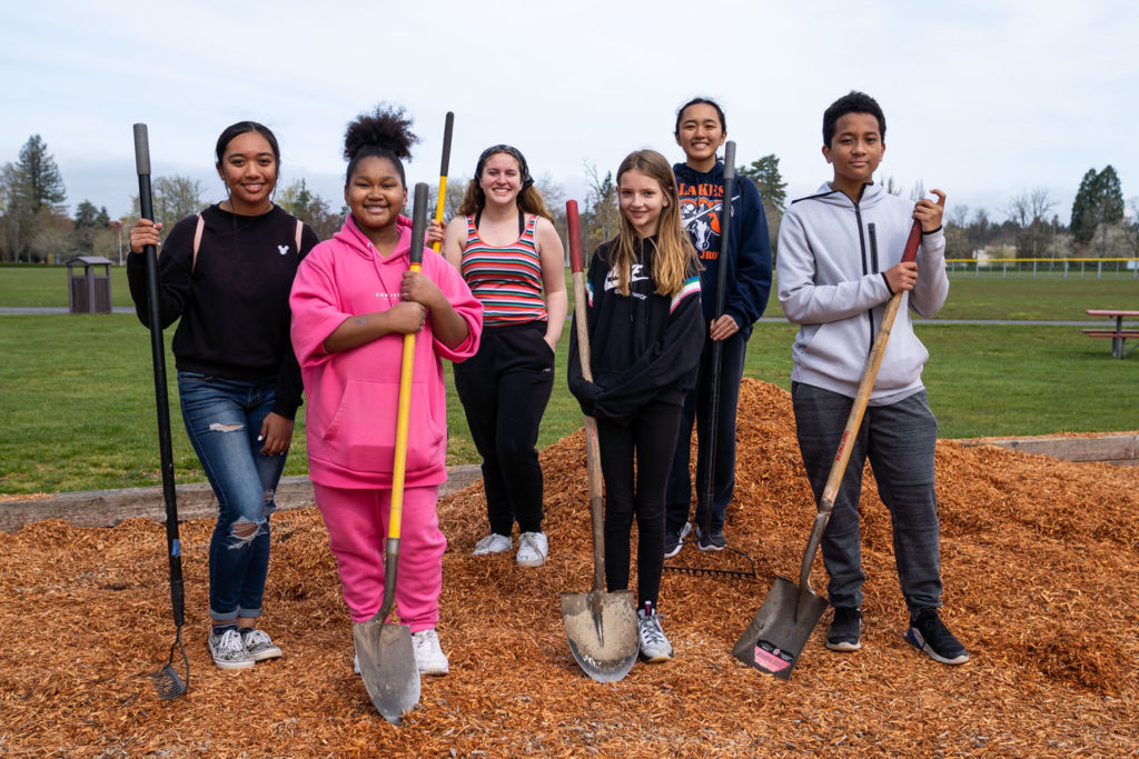 Six student volunteers smile for the camera and stand on a mound of bark. 