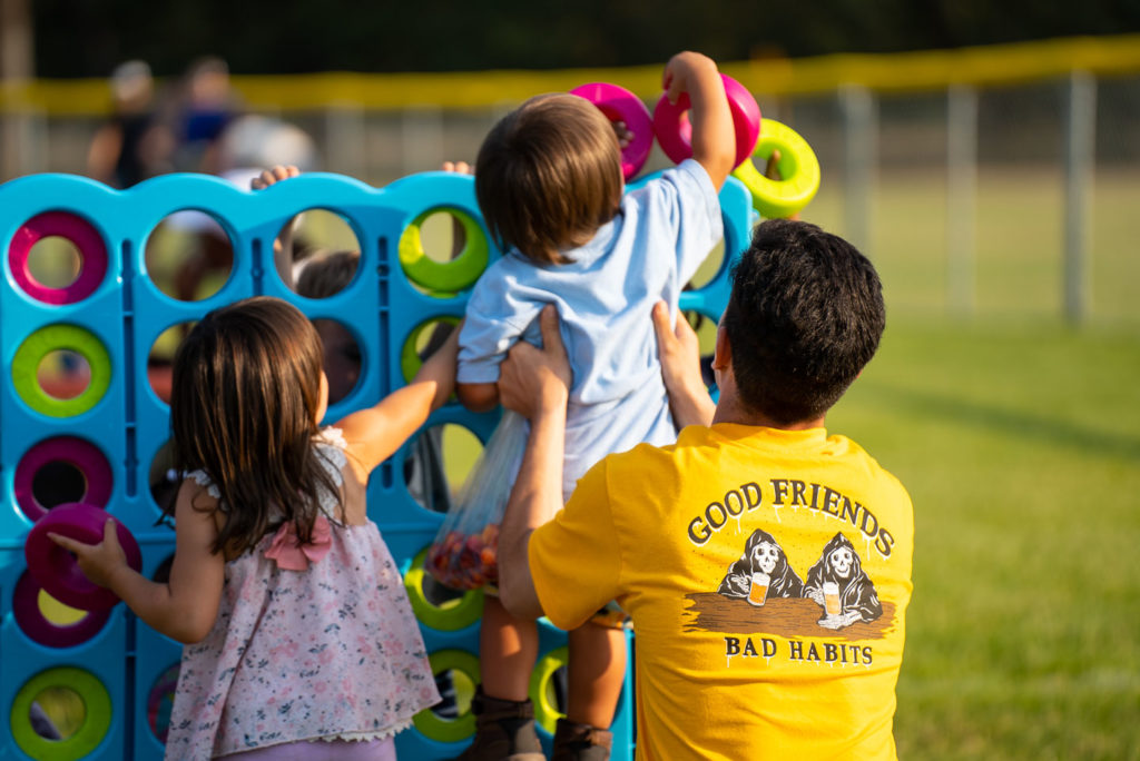 A father lifting his young daughter to put a ring in the jumbo connect-4.