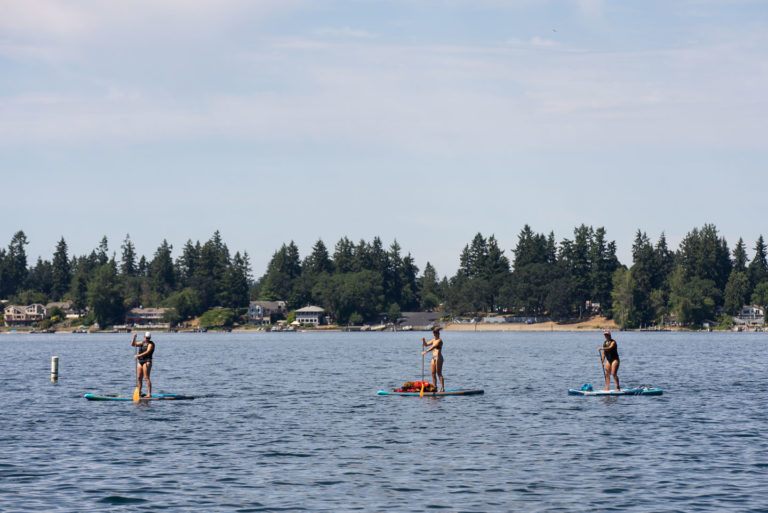 Three paddleboarders enjoy the water at American Lake Park on a sunny day. 