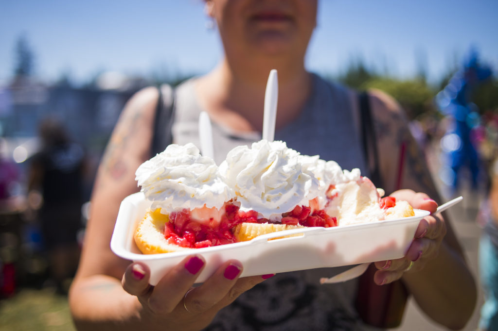 A woman holds a strawberry shortcake toward the camera with whip cream from SummerFEST 2017
