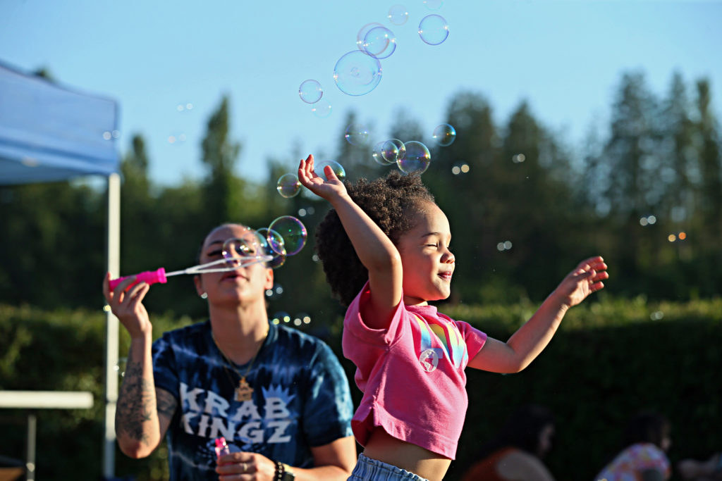A mom blowing bubbles while her daughter runs through them at Lakewood SummerFEST 2022