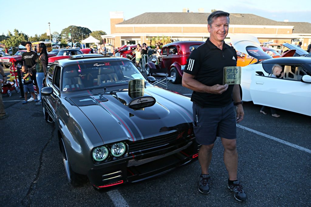 Photo of a man holding a People's Choice sign in front of his custom car