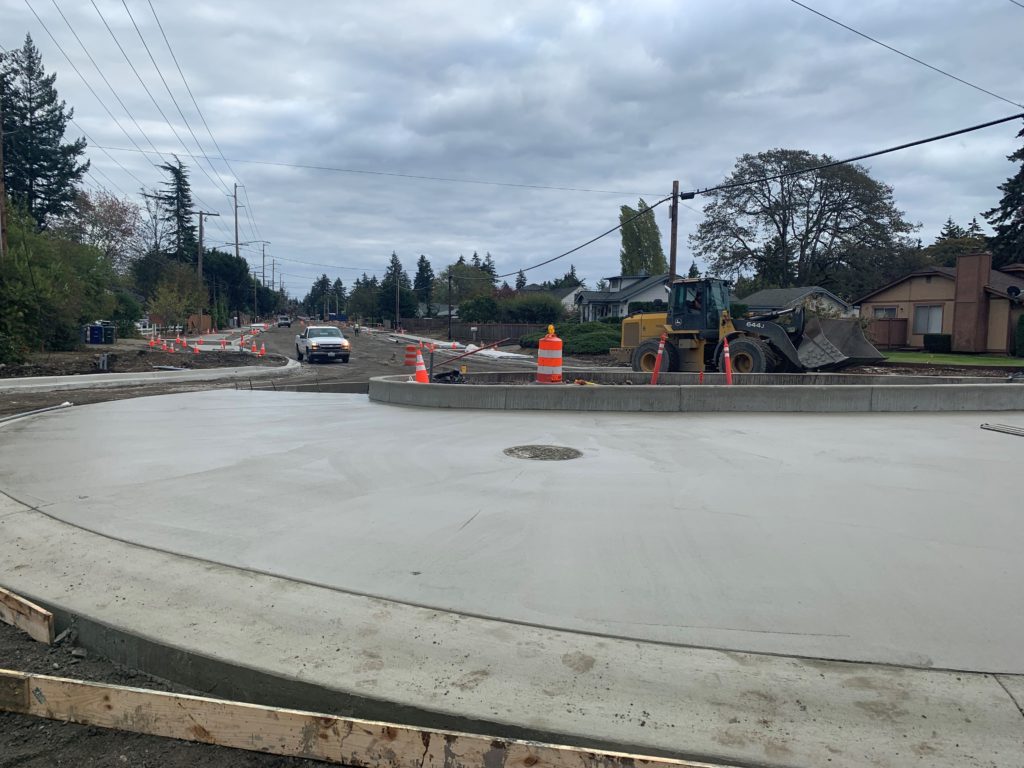 A partially paved roundabout in Lakewood Washington with construction equipment around it.