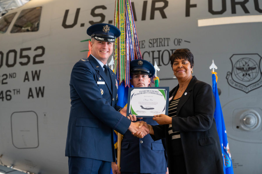 Lakewood Deputy Mayor Mary Moss receiving an honorary commander certificate in front of a large U.S. Air Force plane at McChord Field.