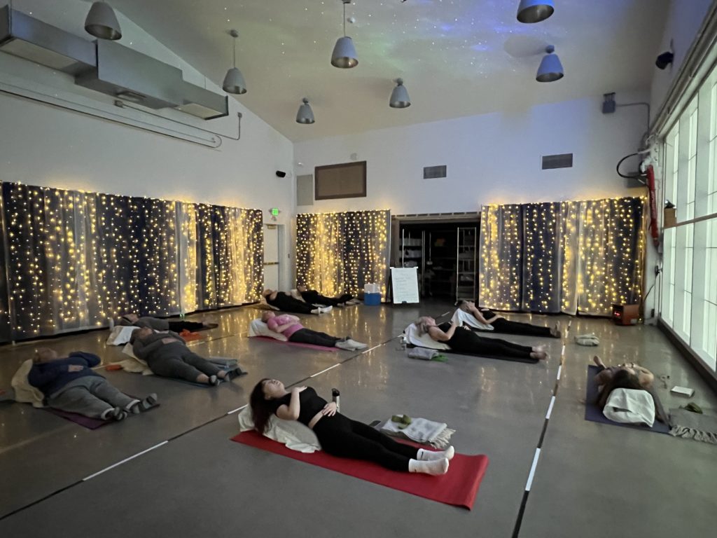 10 people lay on yoga mats while meditating. The room is set with dark mood lighting. 