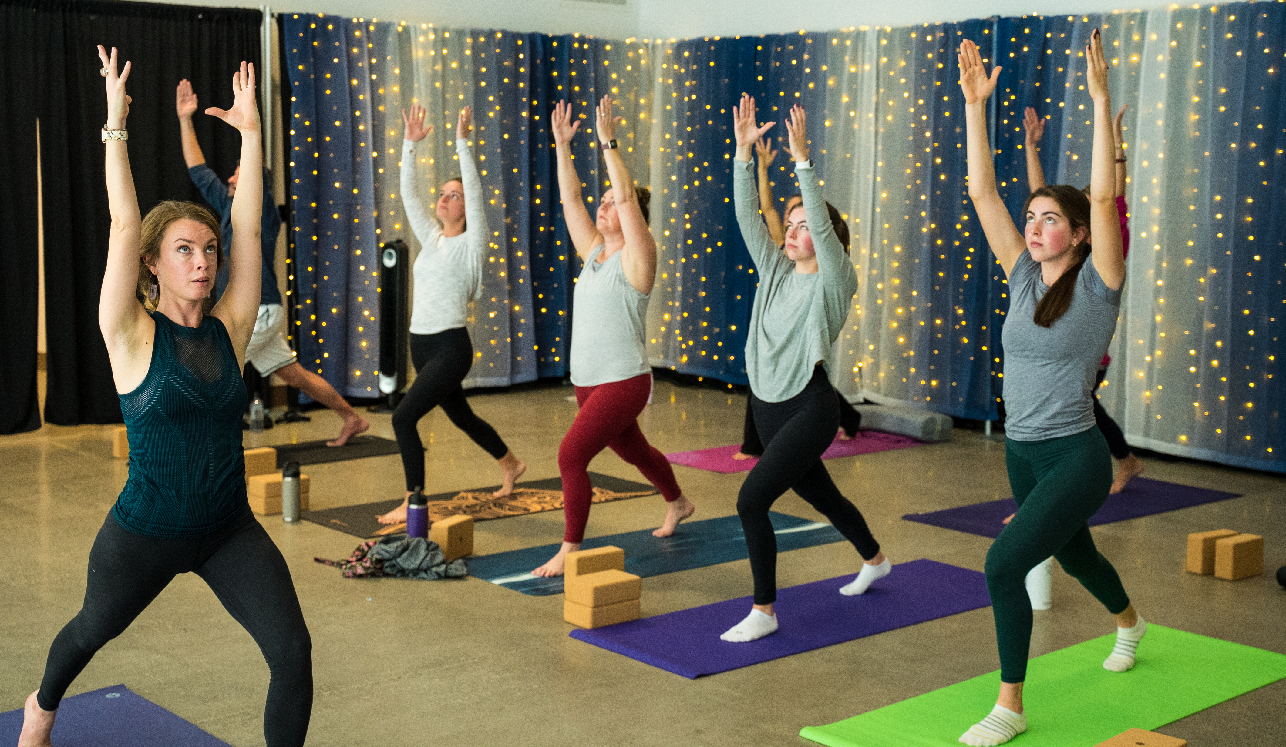 People stand in a row holding a yoga pose with their arms reaching to the air