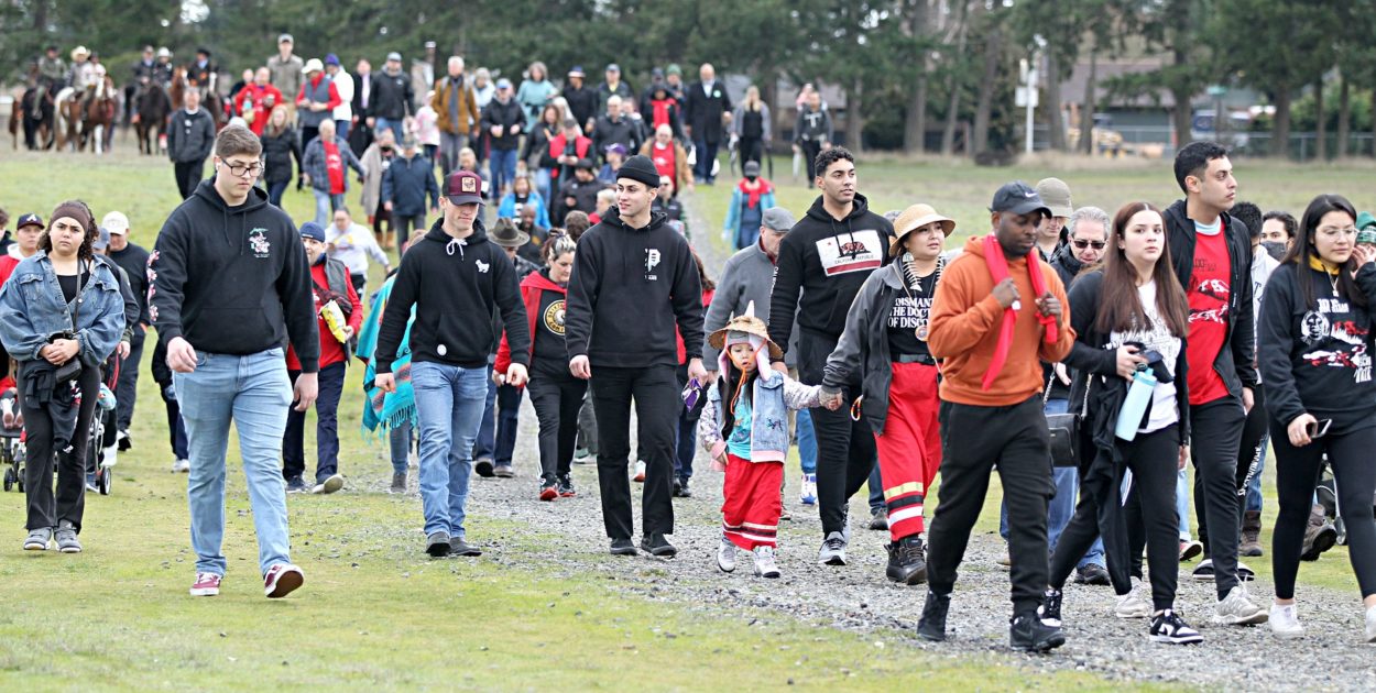 A crowd of hundreds of people walk down a path in Fort Steilacoom Park.