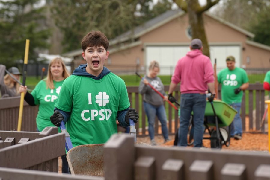 A younger teen pushes a wheelbarrow while making a funny face at the camera.