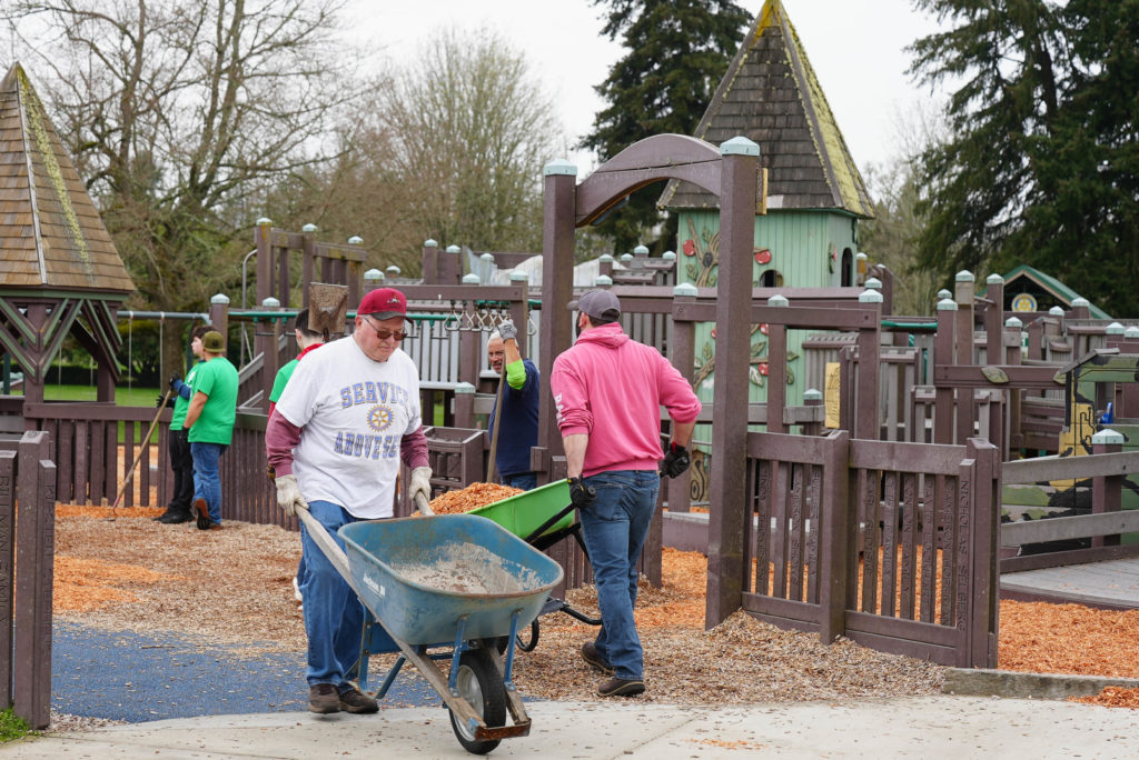 Các tình nguyện viên đẩy xe cút kít chở vỏ cây vào Ft. Sân chơi công viên Steilacoom.