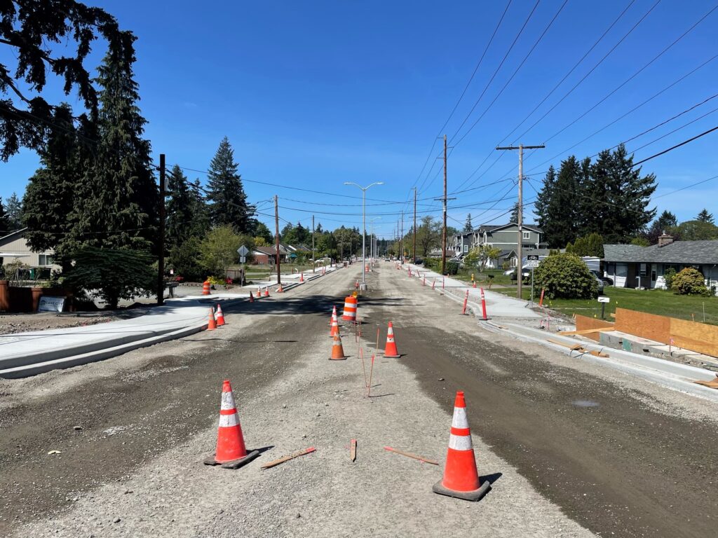 Looking down Washington Boulevard on May 12, 2022. The road is gravel with orange cones lined down the road. Sidewalks are installed.