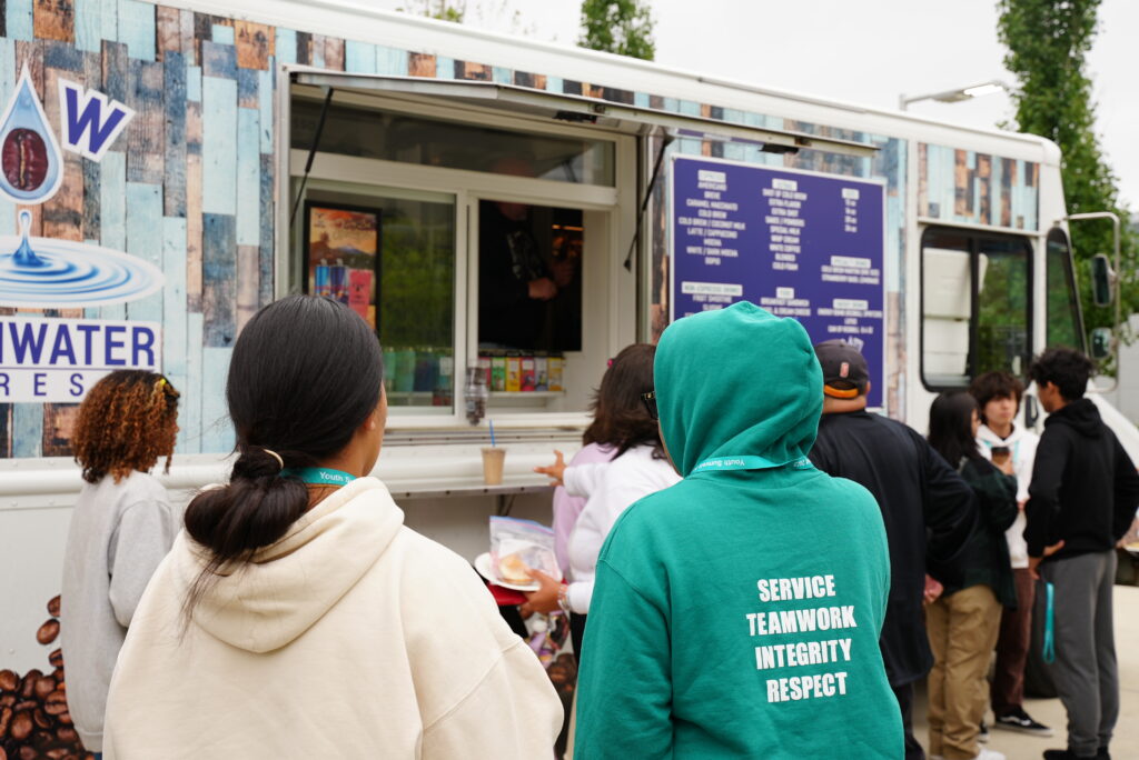 A group of teens wait in line at a food truck.
