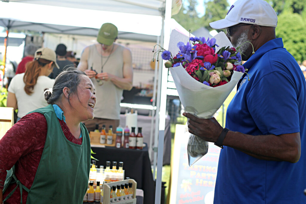 A woman laughs as she talks to a customer at her flower stand at Lakewood Farmers Market.