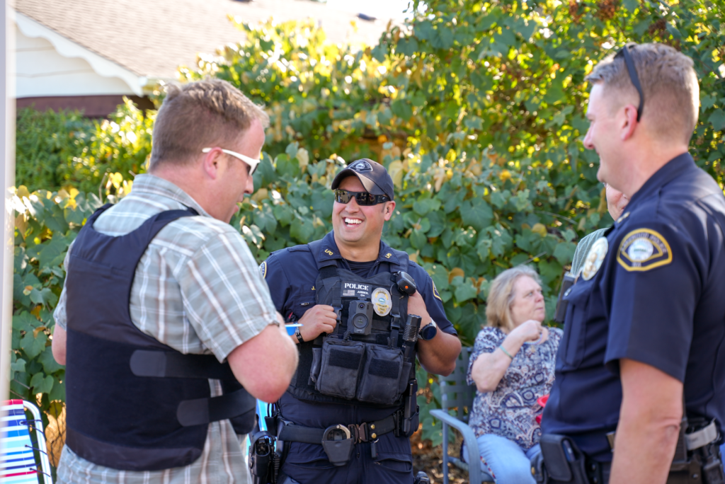 Một sĩ quan cảnh sát Lakewood mỉm cười trong khi những người khác theo dõi sự kiện Đêm hội toàn quốc năm 2023 quanh thành phố vào ngày 1 tháng 2023 năm XNUMX