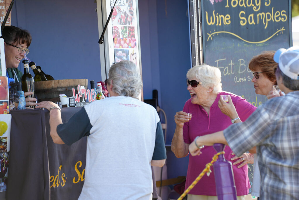 Older women sample wine at the Lakewood Farmers market.