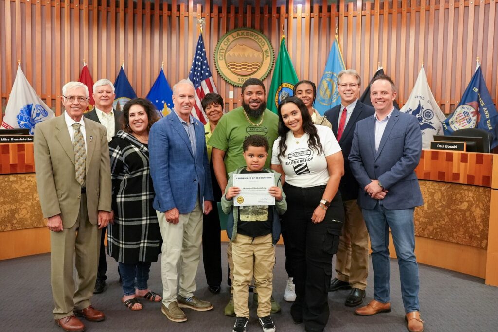 The Lakewood City Council poses with owners of Lakewood Barbershop, JP and Kyro Parker and their children after awarding the September 2023 Lakewood Business Showcase.