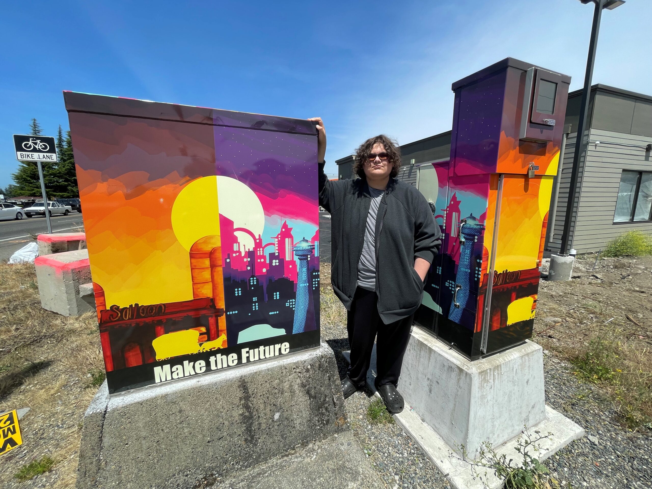 Lakewood high school student Sam Reed poses next to the two signal boxes that hold his artistic design in Lakewood at the corner of 96th Street SW and South Tacoma Way SW.