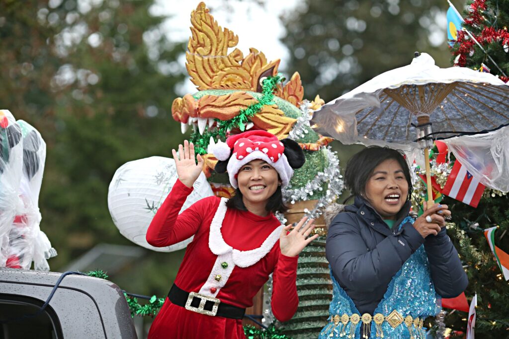 A woman dressed in a red Santa Claus outfit smiles and waves at the camera.