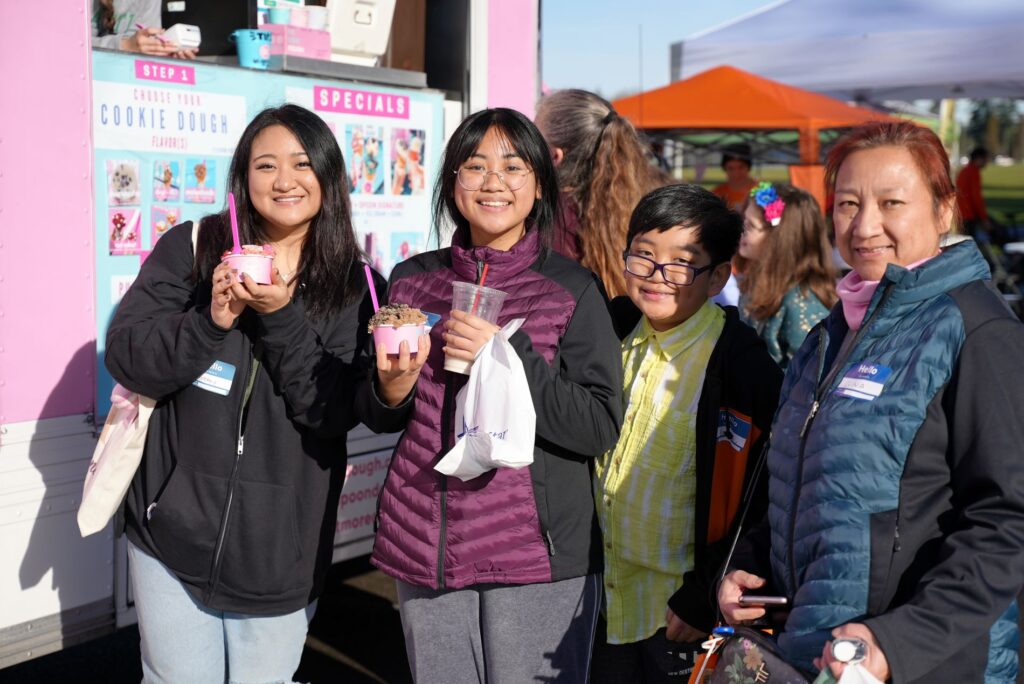A family holds ice cream in cups in front of a food truck at the City of Lakewood 2023 Welcome Walk at Fort Steilacoom Park.