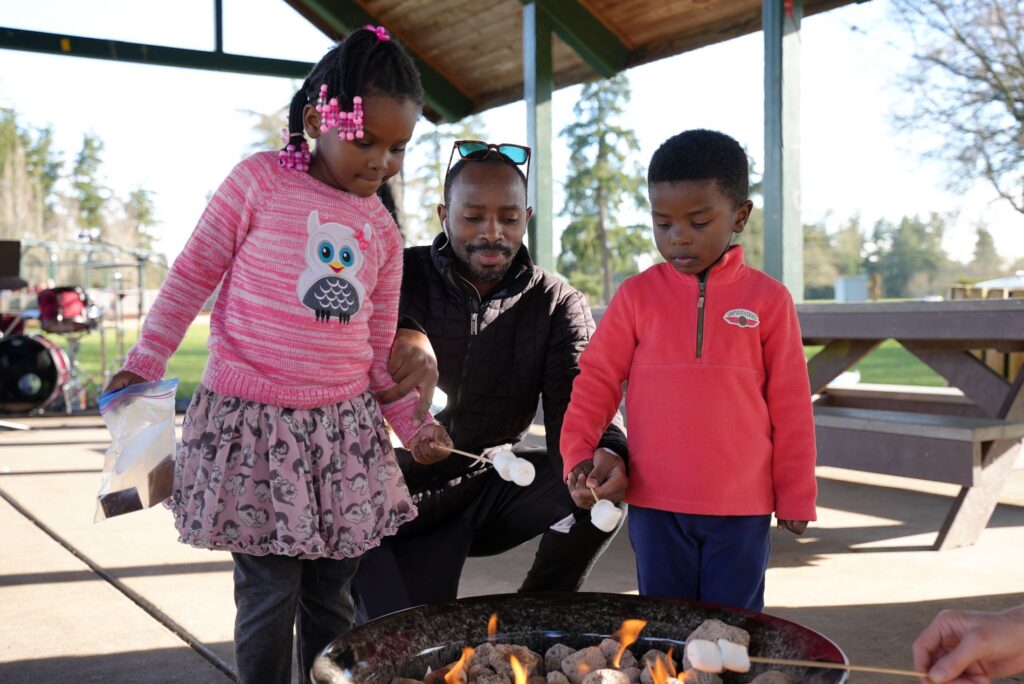 A father with two young children holds marshmallows over a fire pit at Fort Steilacoom Park in Lakewood for the 2023 Welcome Walk event.