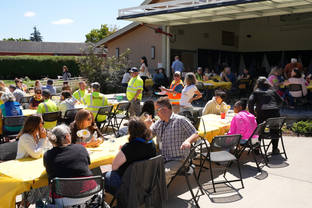 People eat at tables outside of the pavilion on a sunny day. 