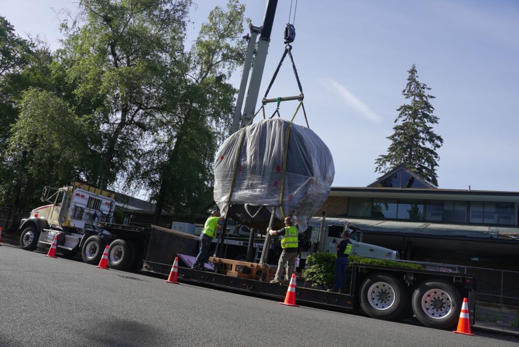 Two people in bright green safety vests help guide the 9-ton Douglas fir round known as The Big One onto a waiting truck on June 13, 2024.