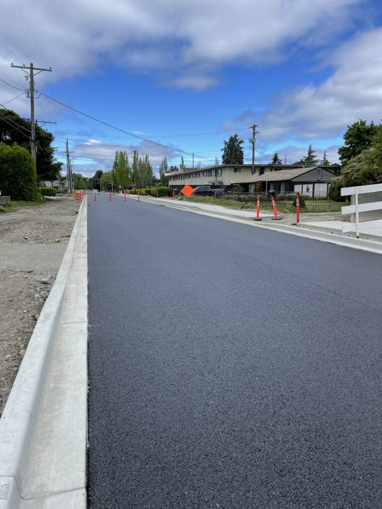 A look down a newly paved Road with new curbs and some orange cones in the distance. This is Hipkins Road in Lakewood, WA.