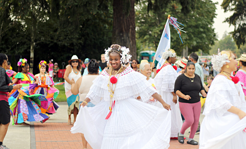 People dressed in traditional Latin American clothing dance outside at a festival.