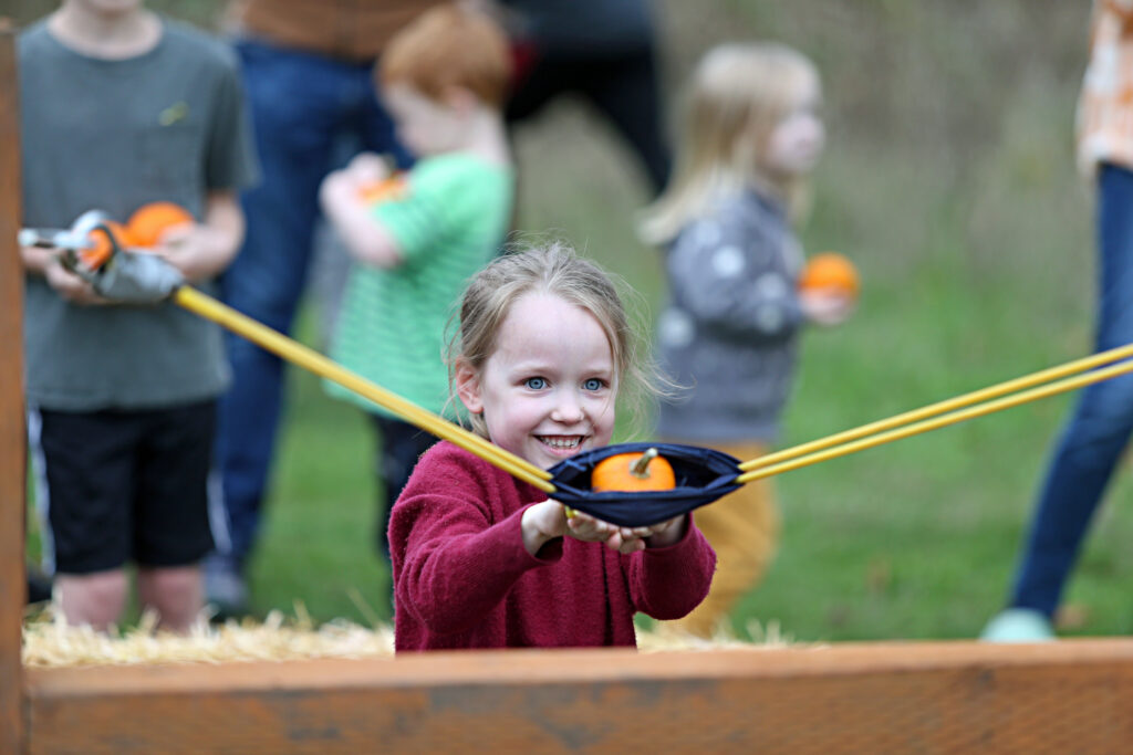 Young girl pulling back a giant slingshot loaded with a small pumpkin.