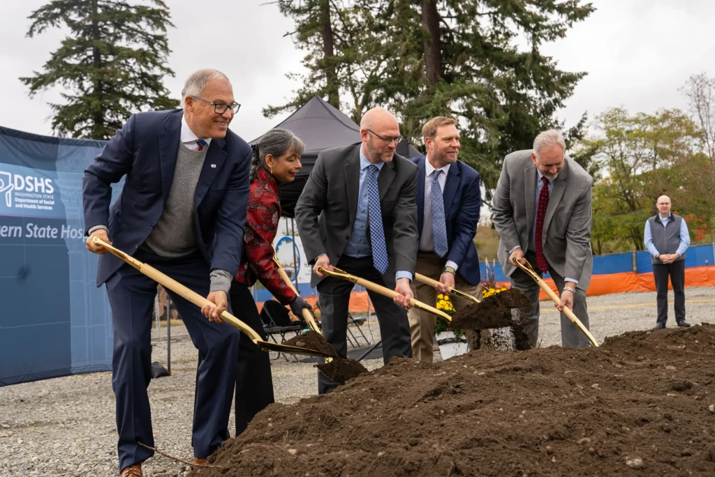 Gov. Jay Inslee and four other people hold golden shovels over a pile of dirt and look up at a camera where they are smiling and posing for a picture. This was taken at the groundbreaking ceremony for Western State Hospital on Oct. 17, 2024 and is a photo by Gov. Jay Inslee's office.