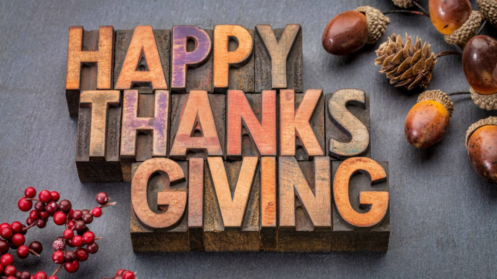 Wooden stamps use letters to spell out Happy Thanksgiving with acorns and small red berries decorating the left and right sides of the card.