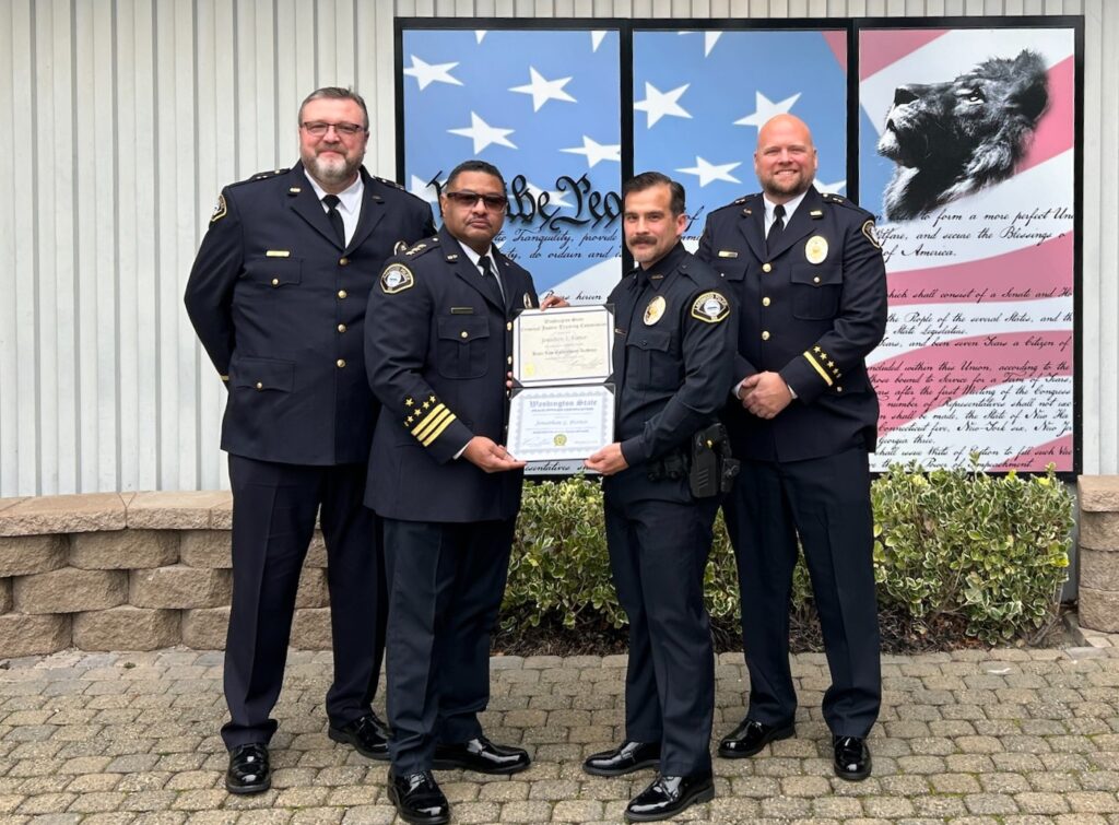 Four members of the Lakewood Police Department pose for a photo in front of the Washington State Criminal Justice Training Center. The Chief of Police Patrick D. Smith and newly hired officer Jon Porter hold up a certificate of graduation.