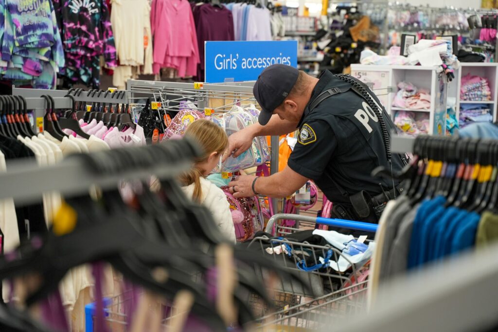 A Lakewood police officer looks through a clothing store rack of items with a young child at the Lakewood Officer's Charity annual Shop with an Officer event on Dec. 22, 2024.