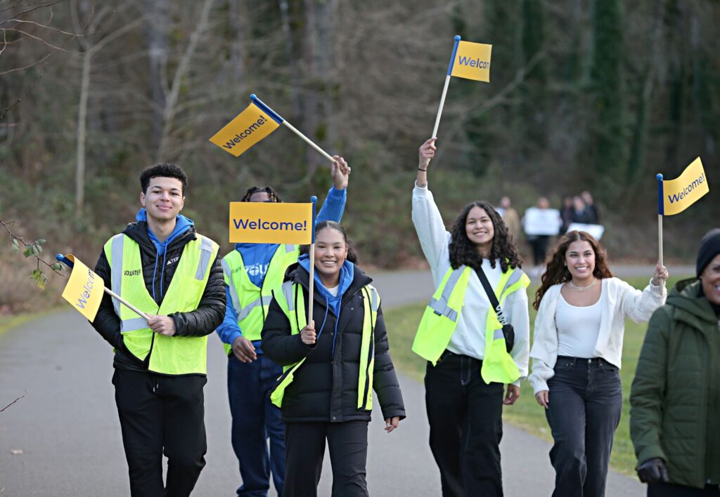 Members of the Lakewood Youth Council wear yellow vests and waive yellow and blue flags with "welcome" written on them as they walk.