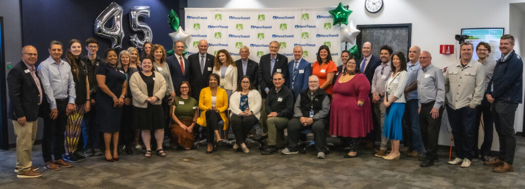 Members of the current and past Pierce Transit Board of Directors stand in a group posing for a photo to celebrate the agency's 45th anniversary