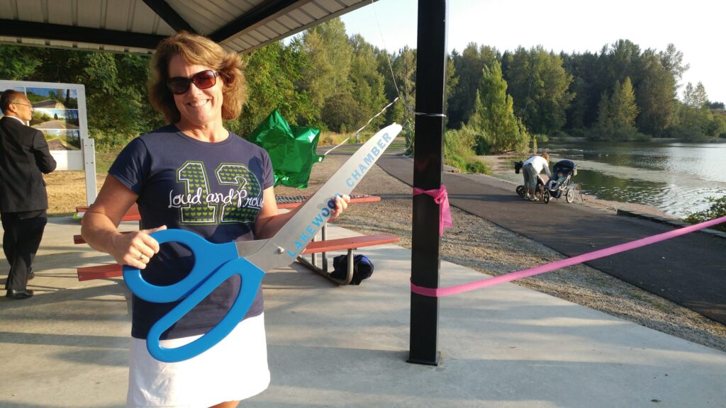 Parks and Recreation Director Mary Dodsworth holds an oversized pair of sciscors and smiles for the camera at the 2017 Waughop Lake paved path ribbon cutting