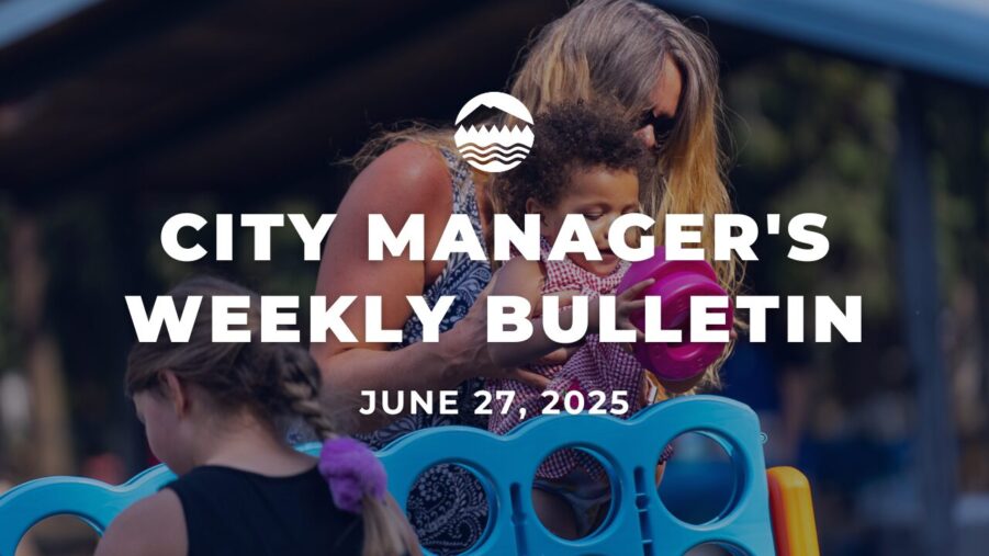 A woman holds a young child in her arms helping the child drop a hot pink "O" into a large Connect 4 lawn game at a city event. White text reads City Manager's Weekly Bulletin June 27, 2025.