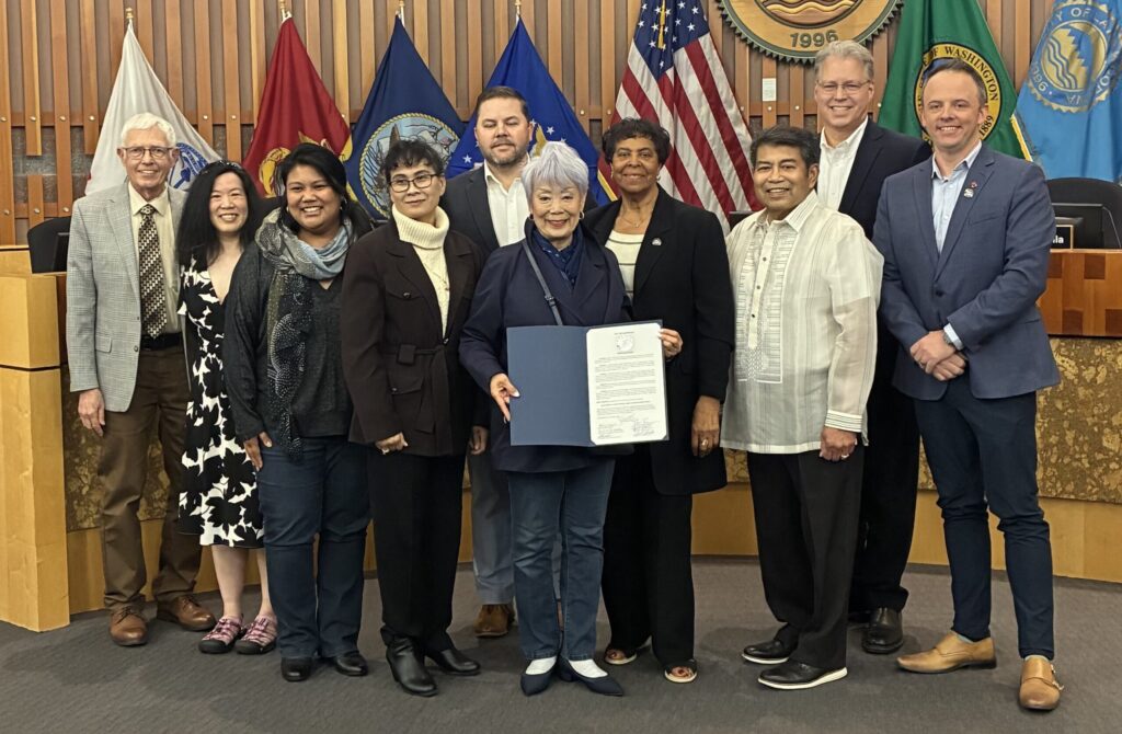 Members of the Lakewood City Council pose with members from the Asian American, Native Hawaiian and Pacific Islander communities after issuing a proclamation recognition May 2025 as Asian American, Native Hawaiian, Pacific Islander Month. They are smiling at the camera from the front of Lakewood City Council chambers.