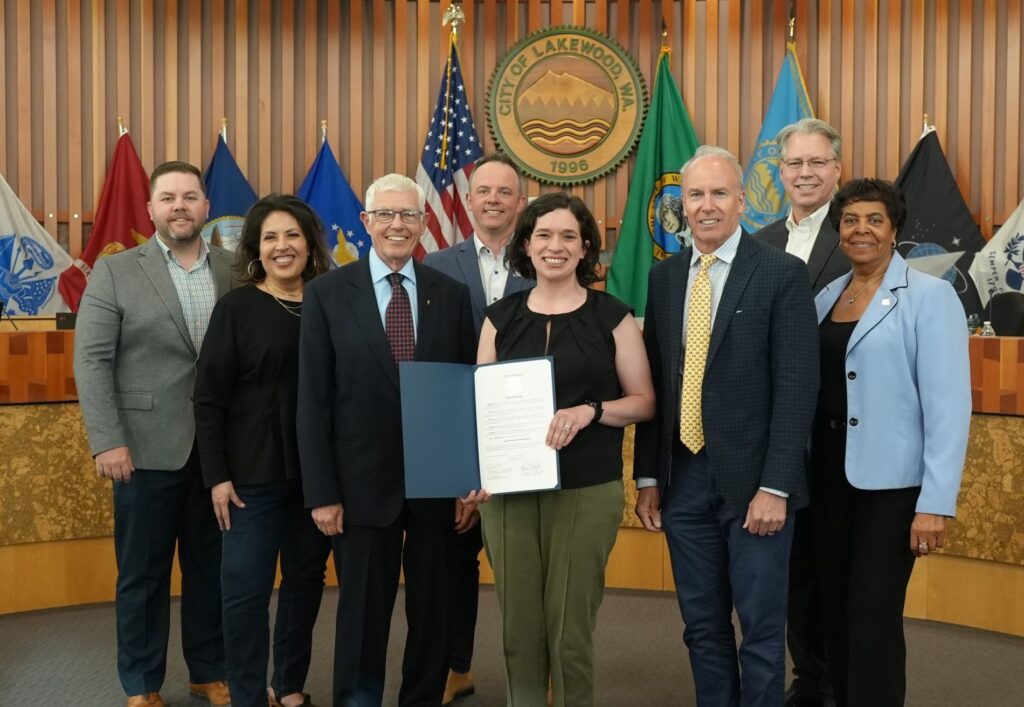 Members of the Lakewood Police Department stand with a representative from Emergency Food Network. They hold a proclamation declaring May 2025 as Hunger Awareness Month.