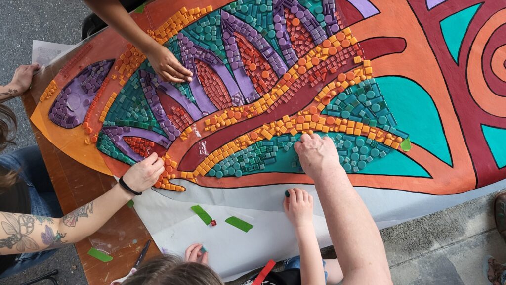 A close of up hands placing colorful tiles on a colorful pattern as part of a mosaic tile project.