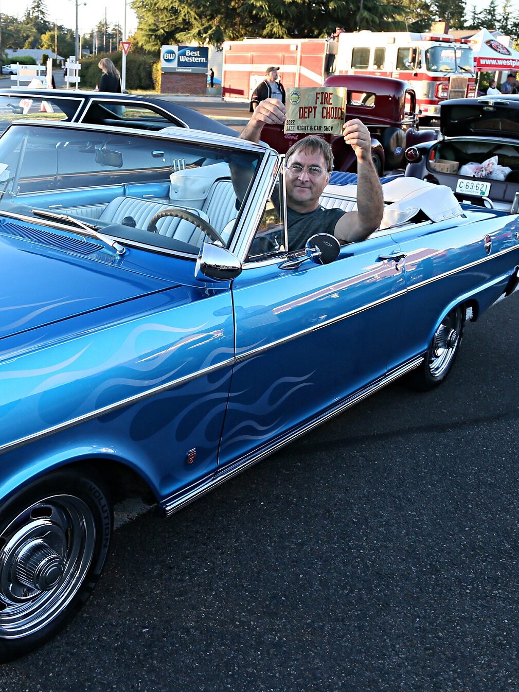 Man seated in custom car holding up Fire Department Choice sign