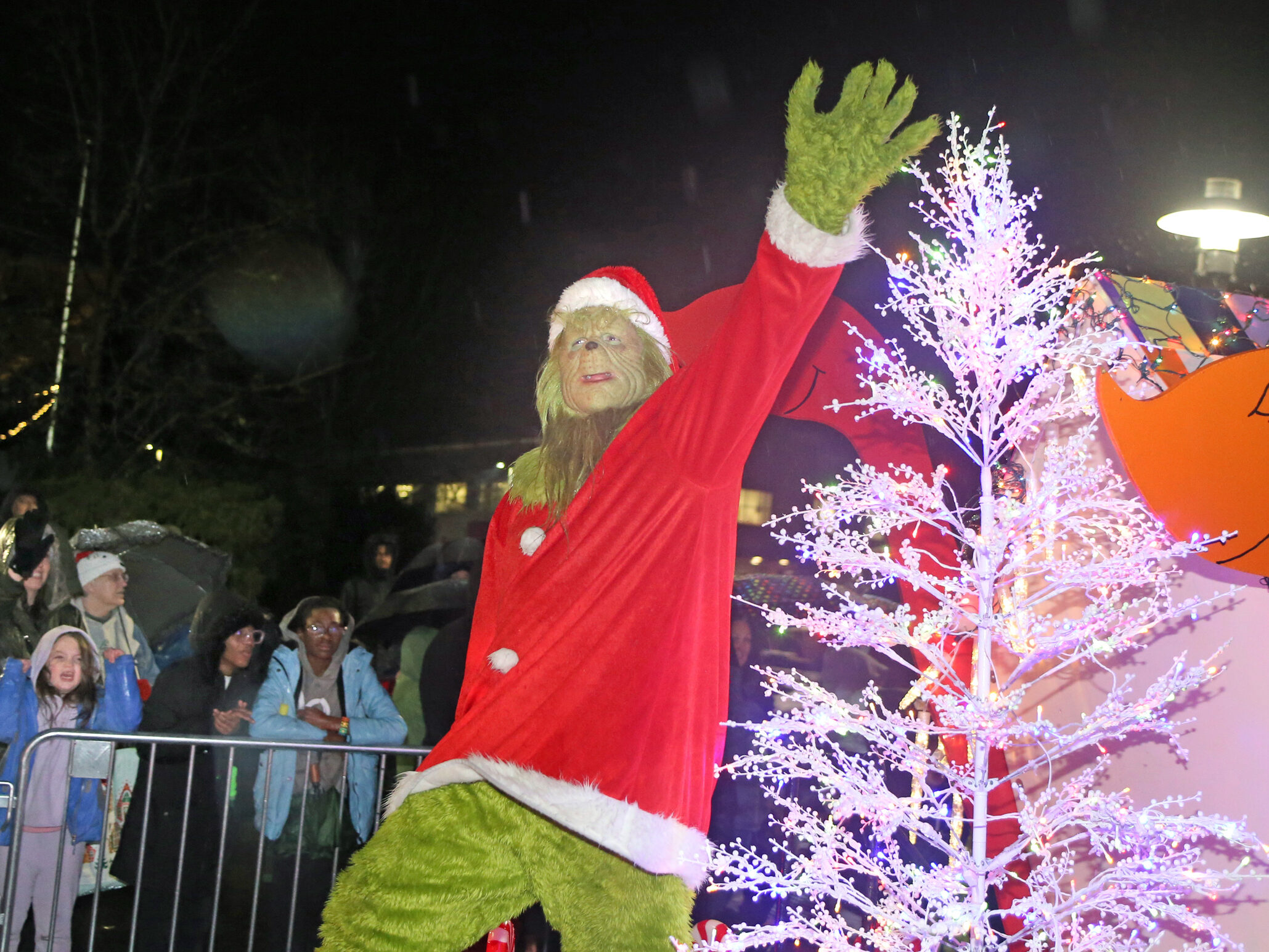 A person dressed in a Grinch costume waves to the crowd while standing on a parade float in the 2023 Holiday Parade of Lights