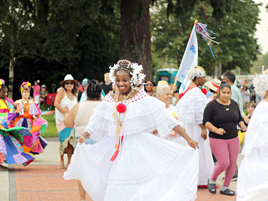 People dressed in traditional Latin American clothing dance outside at a festival.